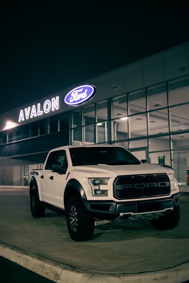 White pickup truck parked outside a Ford dealership at night, showcasing its luxury and modern design.