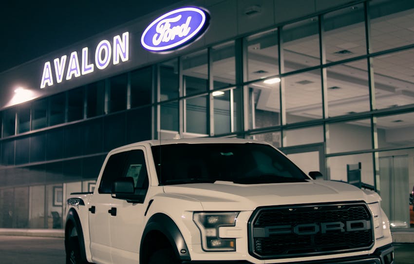 White pickup truck parked outside a Ford dealership at night, showcasing its luxury and modern design.