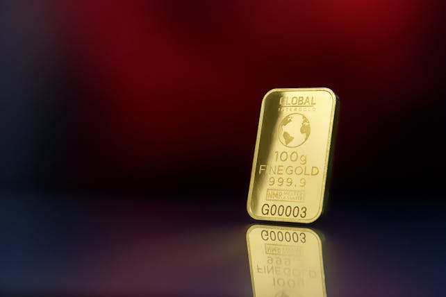 Close-up of a 100g fine gold bar against a red reflective surface, symbolizing wealth and luxury.