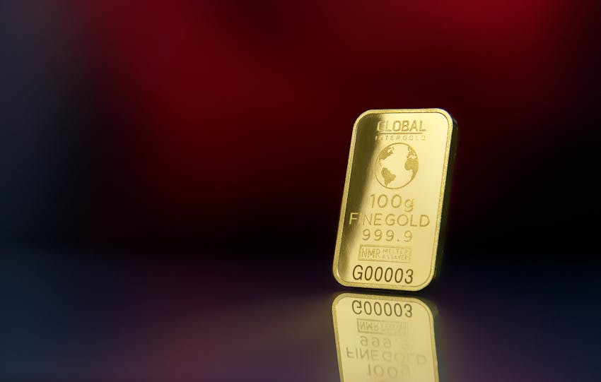 Close-up of a 100g fine gold bar against a red reflective surface, symbolizing wealth and luxury.